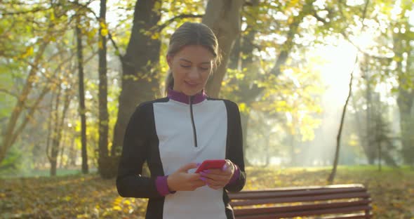 Portrait of Young Woman After Running and Using Smart Phone on the City Park Background.