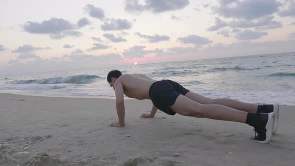 Fit handsome man exercising on beach at sunset performing push ups
