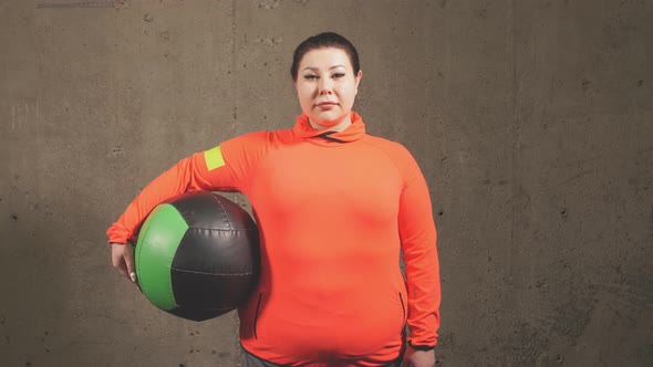 Pleasant Overweight Woman with Exercise Ball Isolated on Gray Background