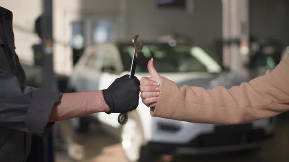 Hand of Auto Mechanic with Wrench and a Female Client Showing Thumbs Up After Repairing a Vehicle