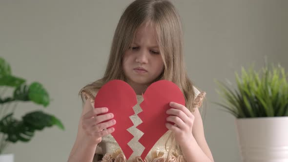 Sad Little Girl Holding Two Pieces of a Red Paper Heart Heartbreak and Heartache Concept