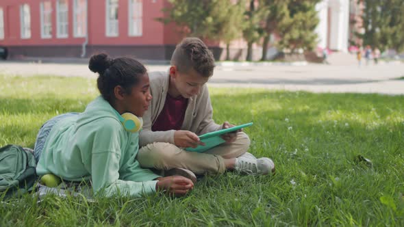 Schoolkids with Tablet Relaxing in Schoolyard