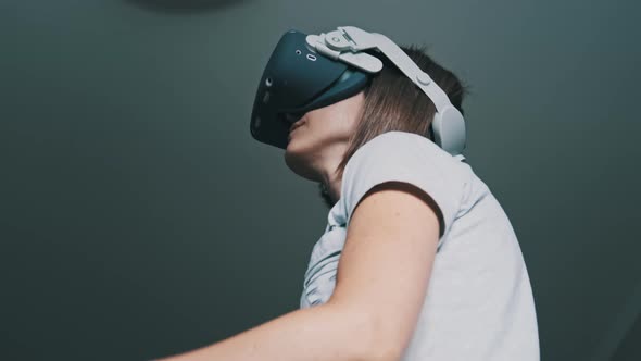 Young Woman in a Virtual Reality Headset Plays a Game at Home