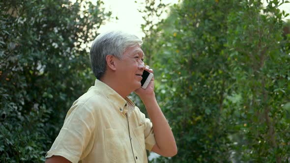 Portrait senior Asian man talking on smartphone happy and smiling outdoors in nature.