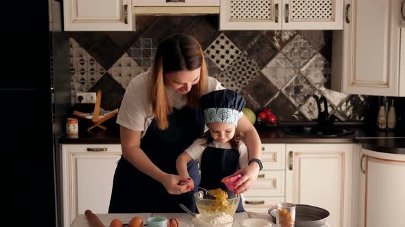 Happy Young Mother with a Small Daughter Prepare Muffins at Home in the Kitchen