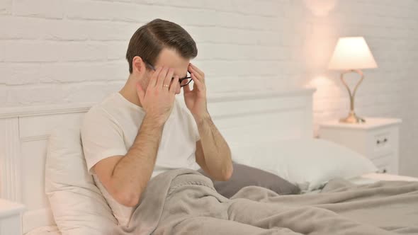 Young Man with Headache Sitting in Bed