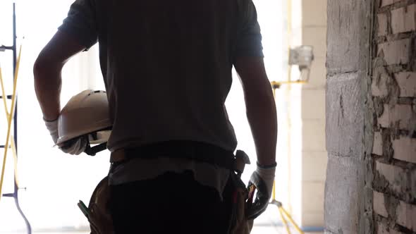 A man builder with a working helmet in his hands at a construction site.