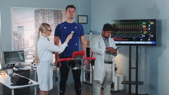 Female Cardiology Technologist Listening To Athlete Heartbeat with a Stethoscope alt