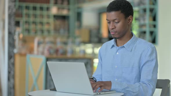 Focused Young African Man Using Laptop in Cafe 