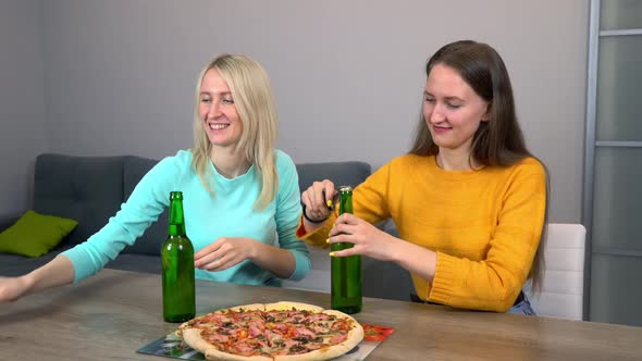 Two best happy girlfriends at home in kitchen eating pizza and drinking beer.