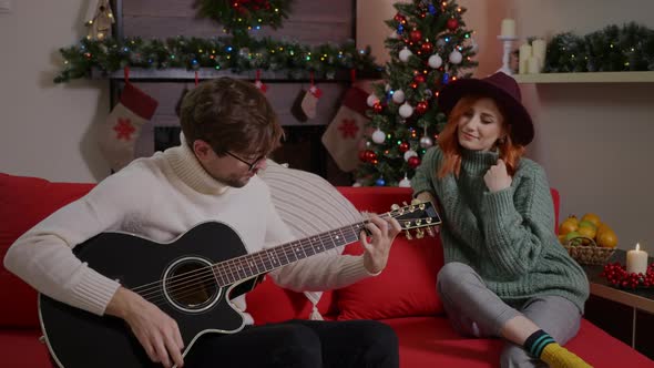 Joyful friends celebrating xmas in good mood, man playing the guitar.