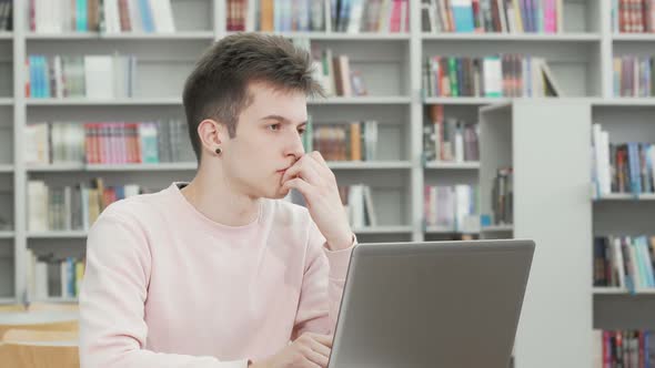 Young Man Looking Thoughtful While Working on a Laptop at the Library