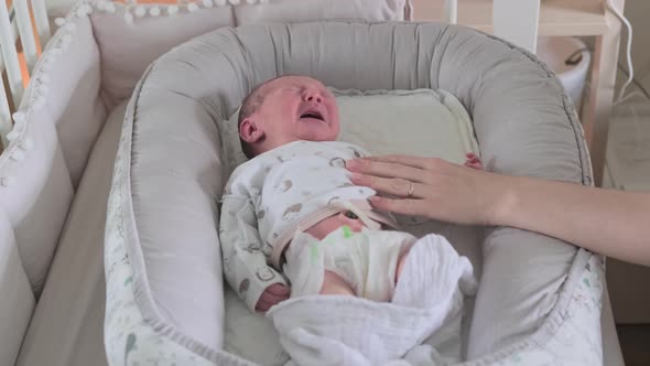 A mother calms a newborn baby in a home crib