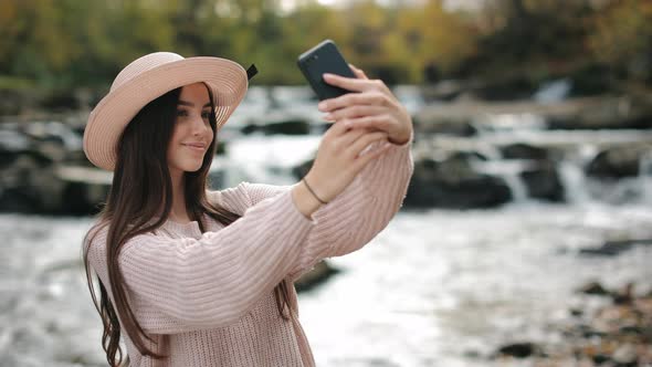 A Young Woman is Taking a Selfie Against the Background of a Mountain River