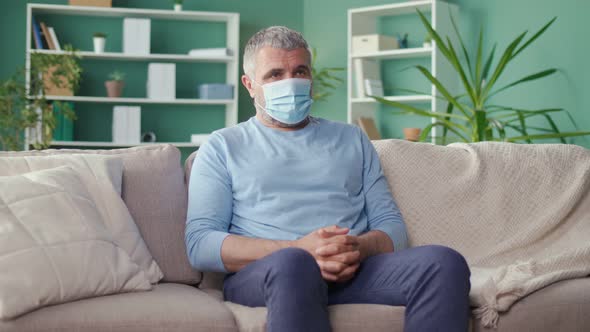 Sad Elderly Lonely Man in a Medical Mask Sitting on the Couch at Home