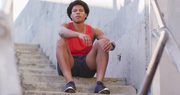 African american man exercising in city, sitting on steps and tying shoelaces