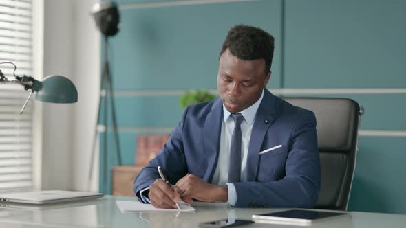 African Businessman Writing on Paper in Office