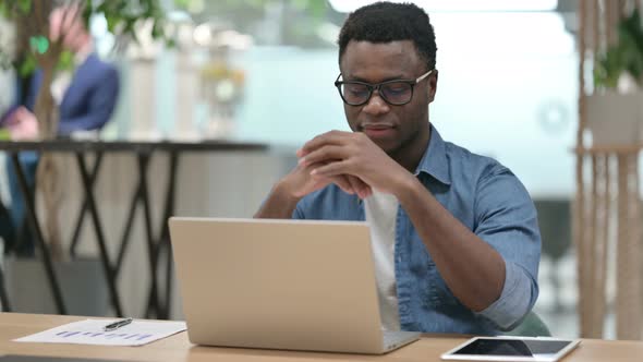 Young African Man Smiling at Camera While Working on Laptop