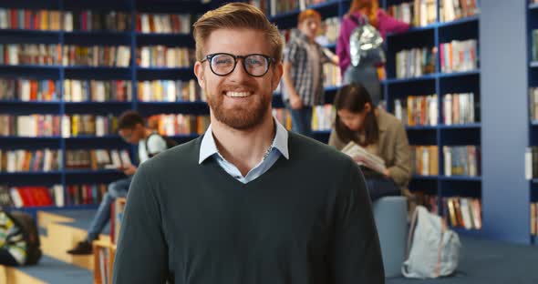 Portrait of Young Male Teacher n Library with Other Students Studying in Background