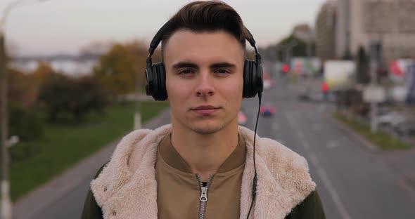 Young Man Listening the Music Puts on Headphones in City