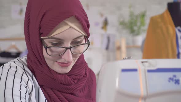 Young Muslim Woman Fashion Designer in National Headscarf Sews on a Sewing Machine Close Up