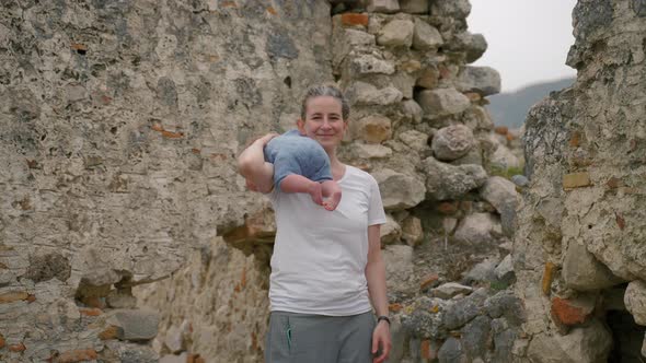 Mother Puts Baby on Shoulder Standing Against Ancient Ruins