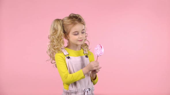 Pretty Girl Is Looking at Pink Candy on Stick. Slow Motion