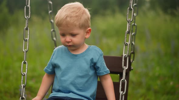 Upset Little Child Sits on Swings Lost at Countryside