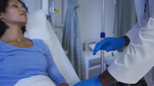 Diverse male doctor preparing drip bag for female patient in hospital room