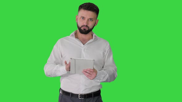 Serious Young Male Executive Using Digital Tablet and Looking To Camera Agreeing on a Green Screen