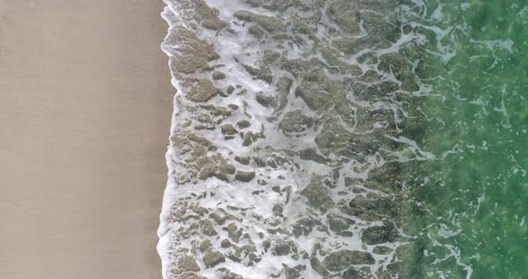 Static top down view of tropical beach, foamy ocean waves washing sand. Waves hitting sand beach