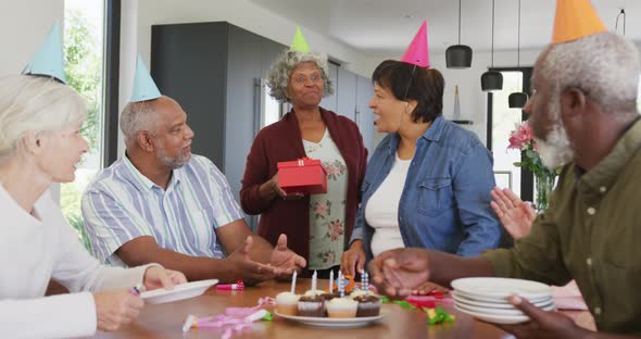 Happy senior diverse people at birthday party with cake and gifts at retirement home