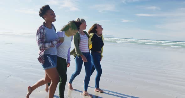 Happy group of diverse female friends having fun, walking along beach