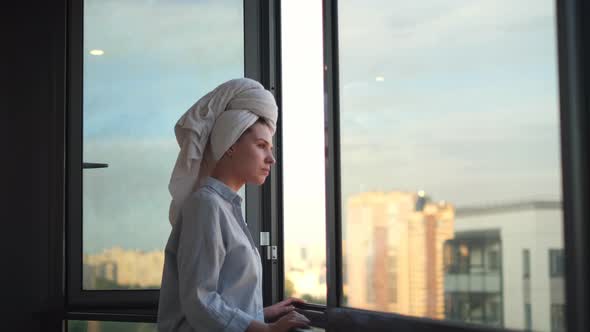 Young woman in a shirt meets the morning on the balcony, daily routine