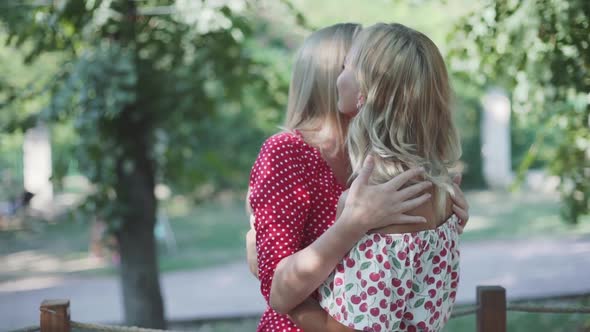 Two Attractive Blonde Girlfriends Talking and Hugging in the Park