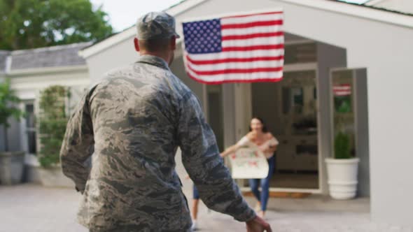 Caucasian male soldier greeting happy son and wife with welcome home sign outside their house