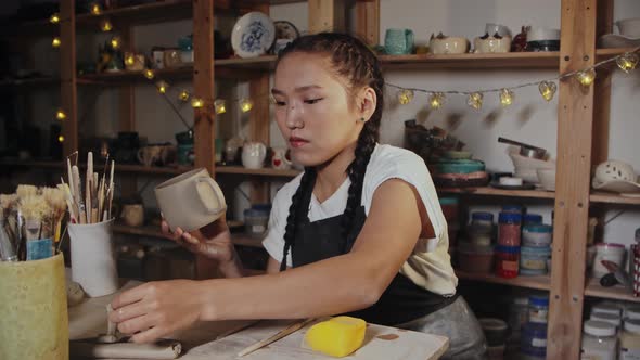 Young Woman Potter Smoothing Out the Clay Cup Using a Wet Brush