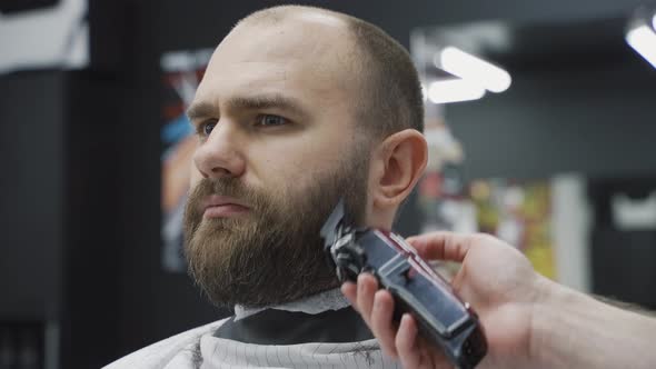 Barber Trimming Bearded Man with Shaving Machine in Barbershop. Hairstyling Process. Close-up of a