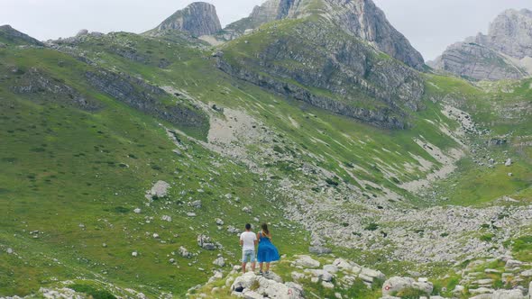 Back View of Young Tourist Couple Holding Hands on Rocky Mountain Top Enjoying Fantastic Panorama