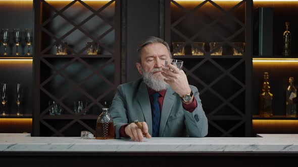 Pensive Mature Bearded Business Owner Resting at Own Cabinet with Glass of Aged Whiskey and Cuban