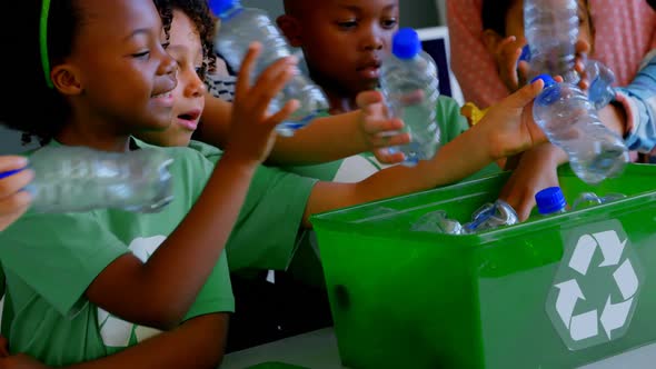 Schoolkids putting bottles in recycle container at desk in classroom 4k