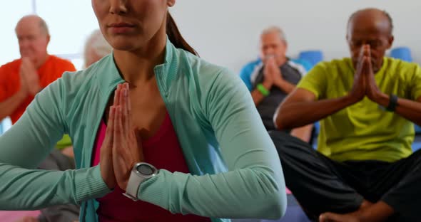 Front view of active mixed-race senior people with trainer performing yoga in fitness studio 4k