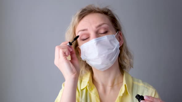 Curly Blonde Joyful Girl in Medical Protective Mask Paints Eyelashes Does Makeup