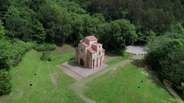 Drone zoomed out revealing a large ancient pre-Romanesque church in the middle of a green forest. Da