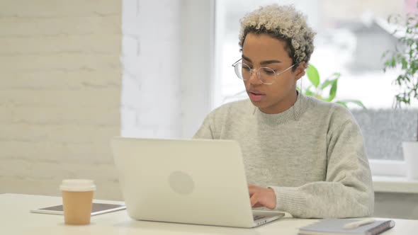 African Woman Looking at Camera While Using Laptop in Office