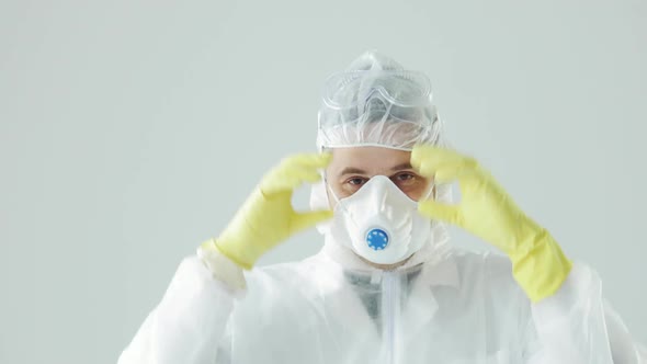 Doctor in Protective Suit Takes Off Respirator and Glasses, Looking at Camera.