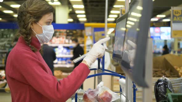 Woman in a Medical Mask and Rubber Gloves Weighs Apples on an Electronic Scale in a Supermarket