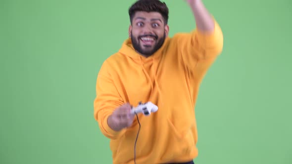 Happy Young Overweight Bearded Indian Man Playing Games and Winning