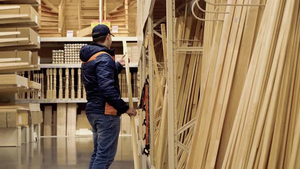 Young Guy Chooses Wooden Beams in Building Materials Store.