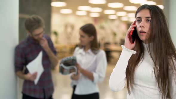 Portrait of Young Girl Worried Talking By Telephone in Working Place on the Background of Chatting